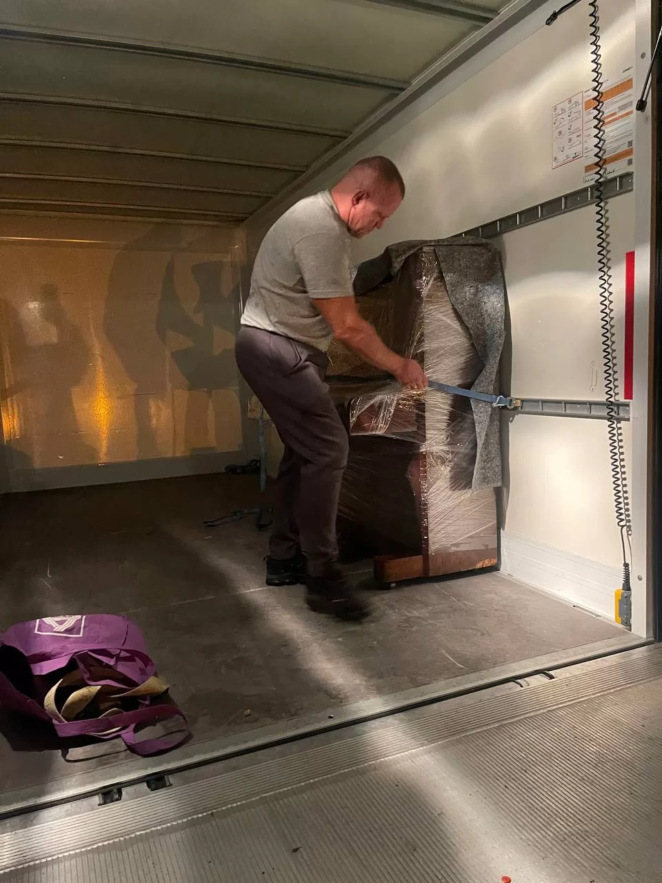 Momot Umzug Mitarbeiter sichert ein Klavier im Umzugsfahrzeug